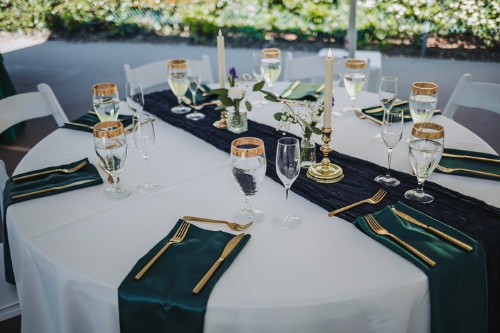 A reception table with green linens, gold flatware, and white flowers