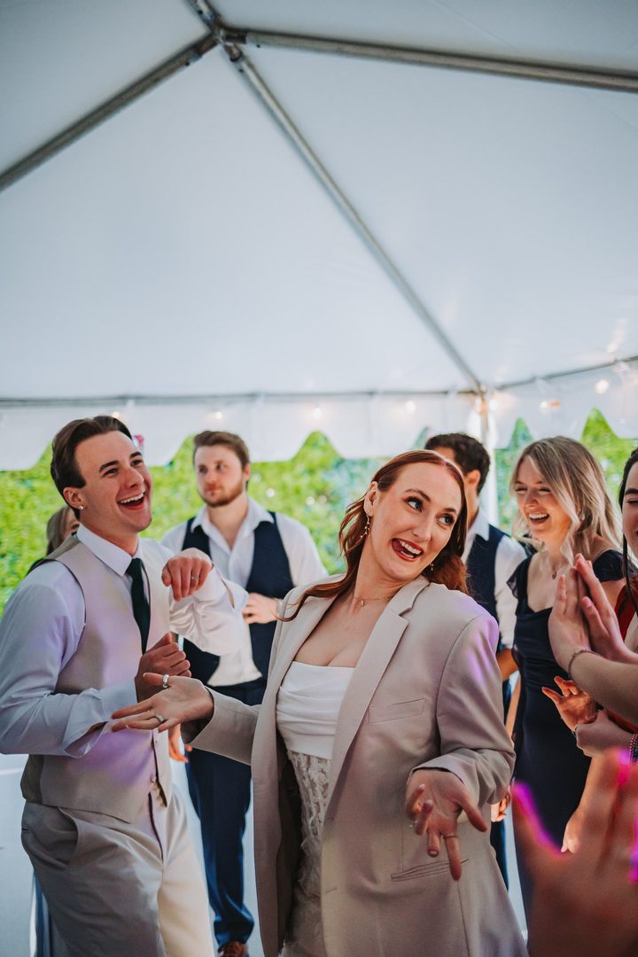 Max and wedding guests laughing beneath the reception tent