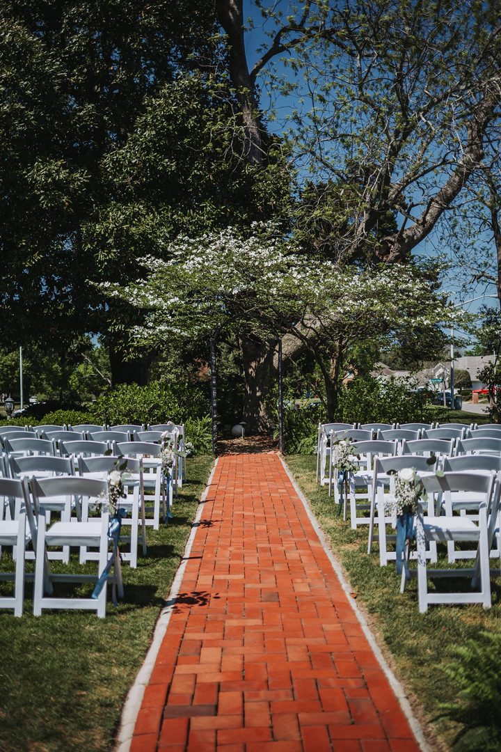 The brick garden aisle lined with white ceremony chairs