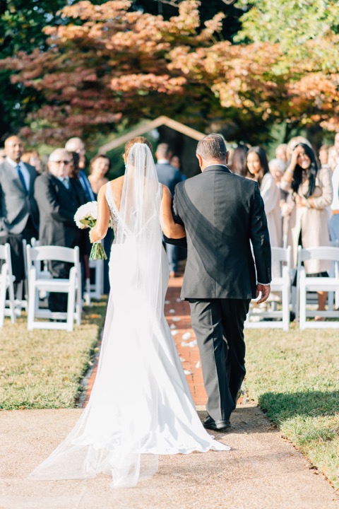 The bride walking toward the flower-filled ceremony arbor
