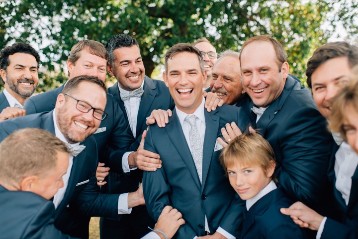 The groom laughing with his wedding party in the gardens