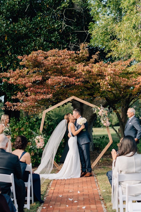 The couple sharing a kiss beneath the ceremony arbor