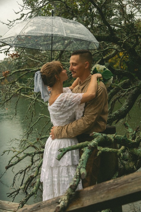 Kali embracing Casey beneath a clear umbrella