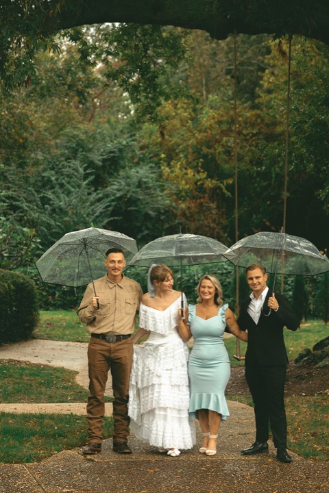 Casey and Kali posing with family under umbrellas