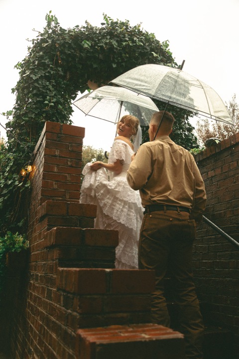 The couple walking beneath an umbrella by the garden archway