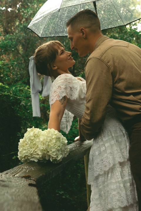 The couple embracing beneath the trees and their umbrella