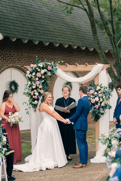 Tyler and Kate exchanging vows beneath the floral arbor