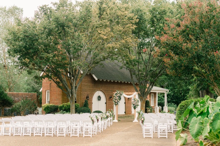 White ceremony chairs beneath the trees by the Carriage House