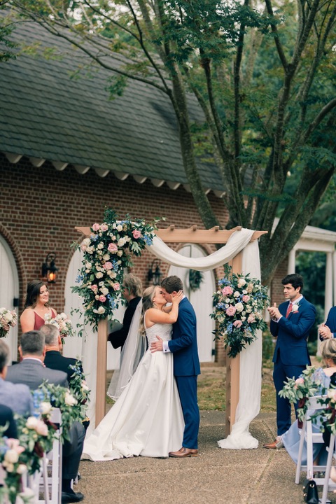 The couple sharing a kiss beneath the ceremony arbor