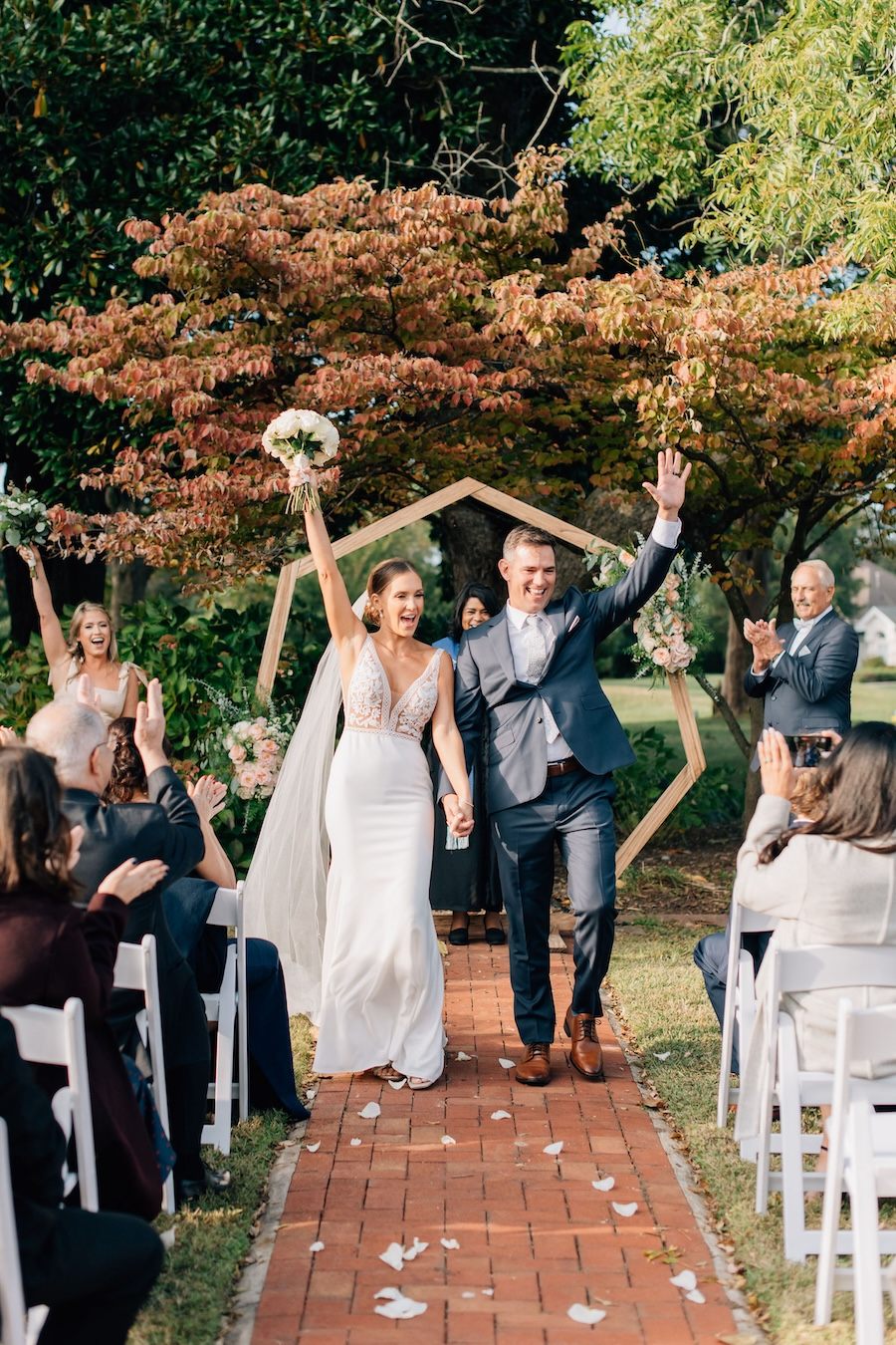 Newlyweds smiling and raising their arms as they walk back down the garden aisle