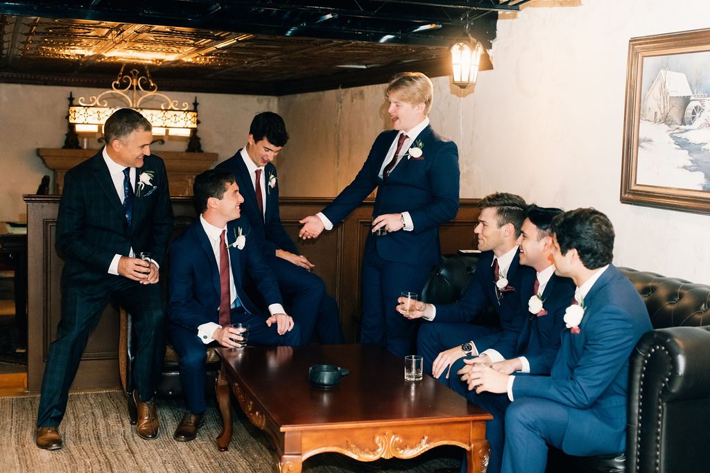 The groom and his friends chatting together on antique leather sofas in the Cellars