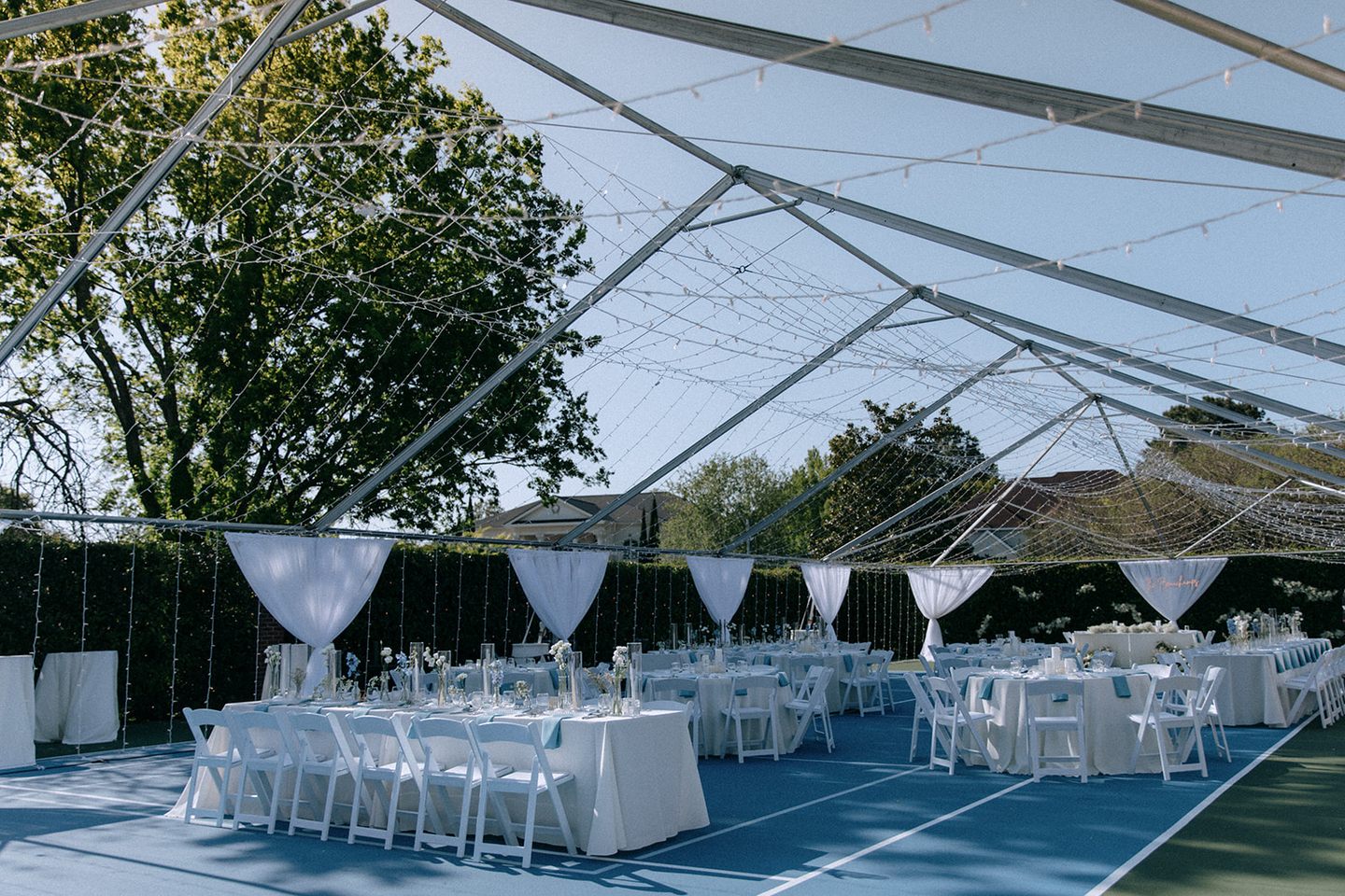 A wedding reception beneath a clear tent, with white draping and round tables