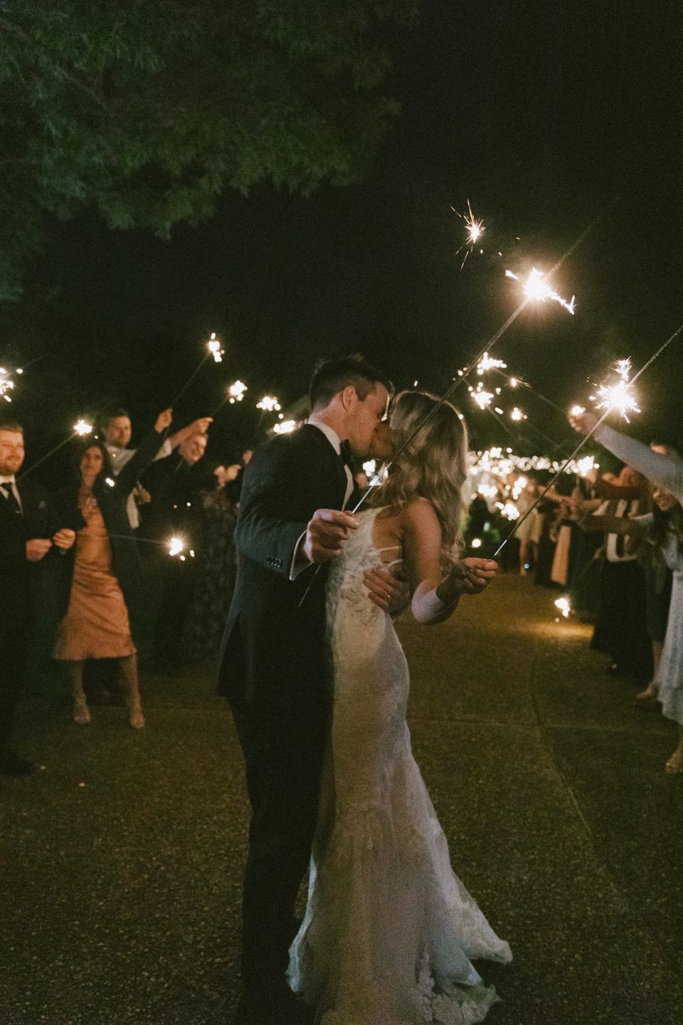 The newlyweds kissing as their guests hold sparklers for an evening send-off