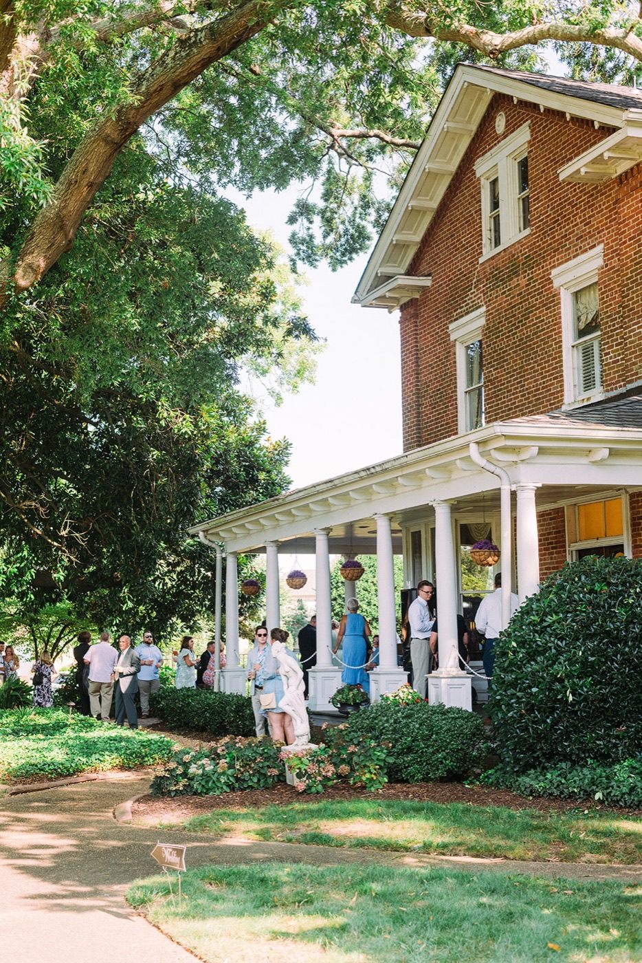 Wedding guests gathering on the shaded lawn beside the Manor’s veranda